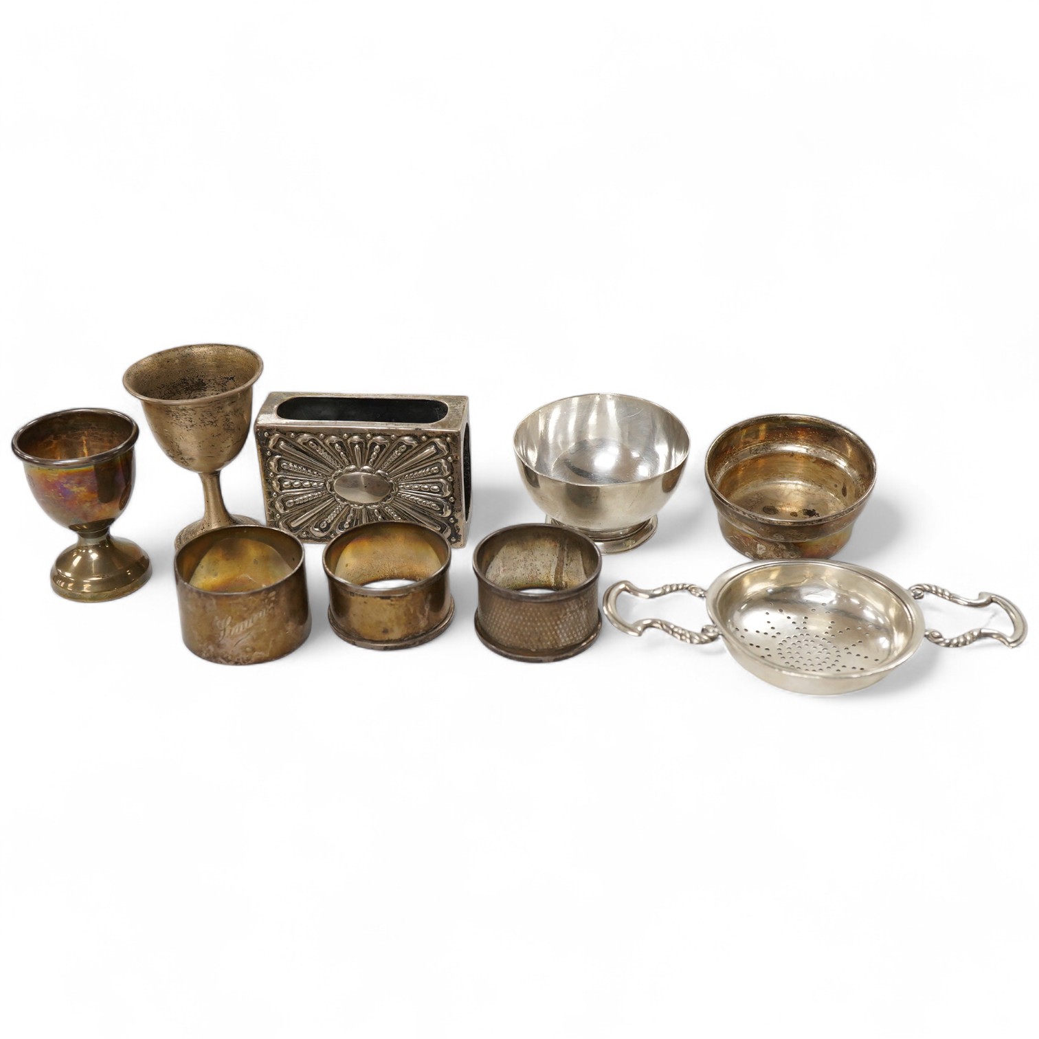 Sundry silver, consisting of - a modern tea strainer and stand, bu C.J. Vander Ltd, an egg cup, small goblet, three serviette rings, a stand and a match box case.